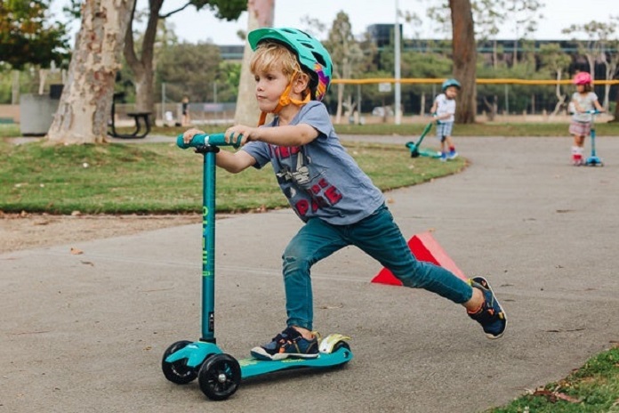 a kid and two kids in background having fun in park with scooters