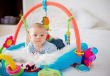 Cute baby boy on colorful gym, playing with hanging toys at home