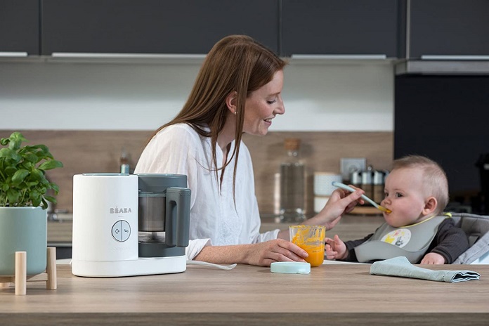 mom feeding baby from baeba baby food steamer and blender on table