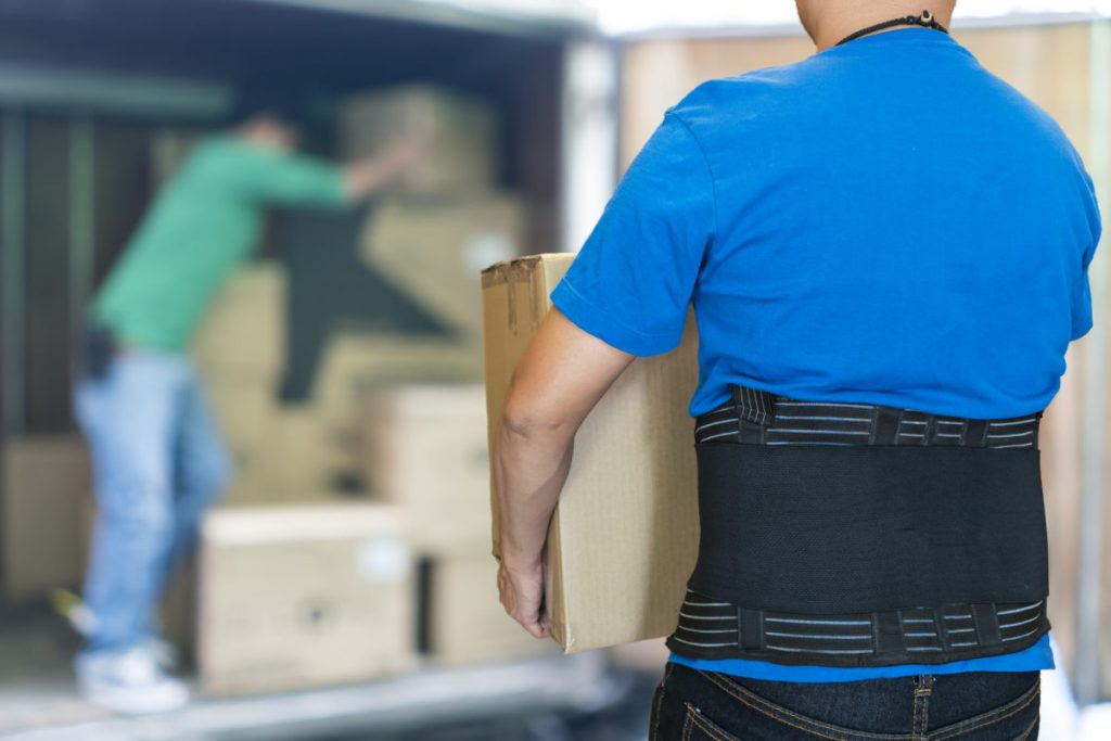 Man lift heavy carton wearing support belt for protect his back, blurred background of worker lift cartons
