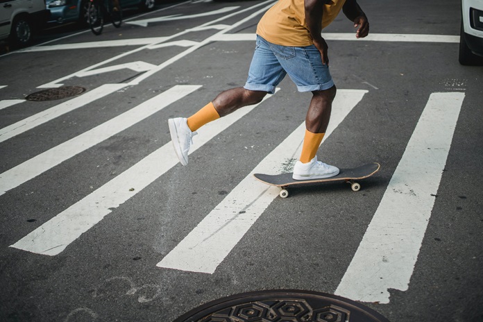 skater crossing a crosswalk with his skateboard