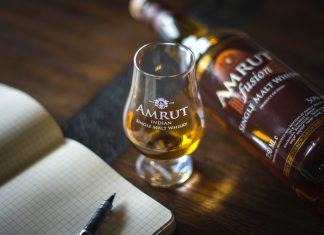 Amrut Indian single malt whisky with a glass and a notebook on a wooden table.